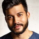 Close-up portrait of a handsome man with a beard in casual attire, smiling warmly.